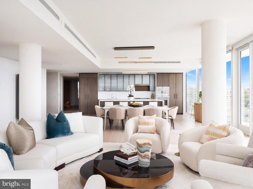 Open-plan living room and kitchen with curved white seating, wood cabinetry, and large windows.
