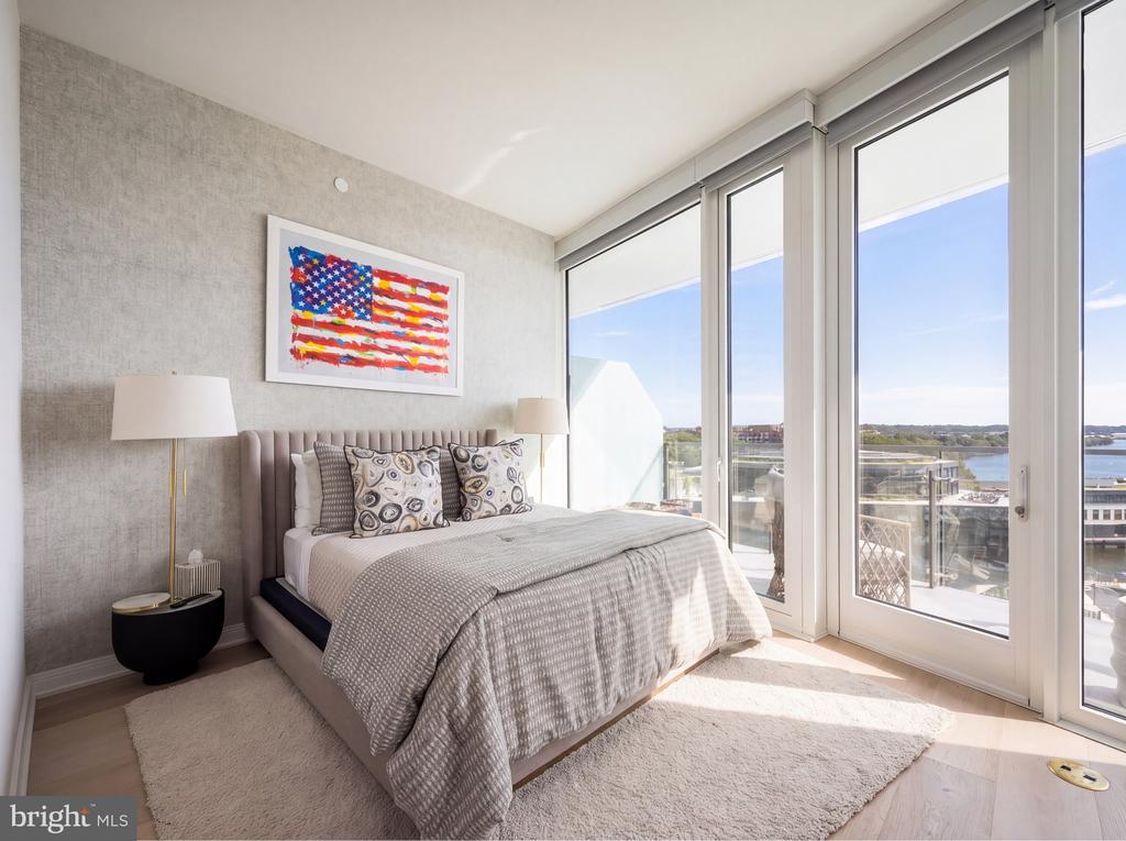 Bedroom with floor-to-ceiling windows overlooking water and a balcony.