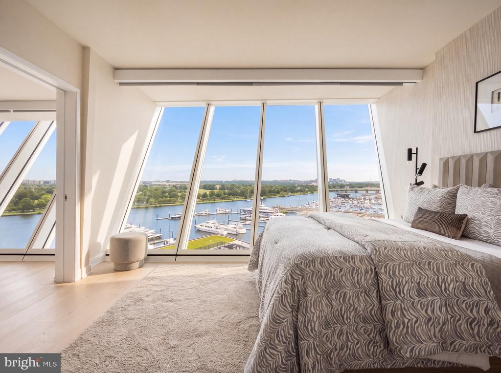 Bedroom with a patterned bedspread and angled windows overlooking the river and marina.