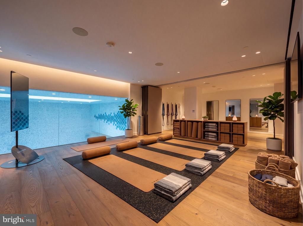 Fitness studio with yoga mats, bolsters, and towels beside a blue-lit glass wall.