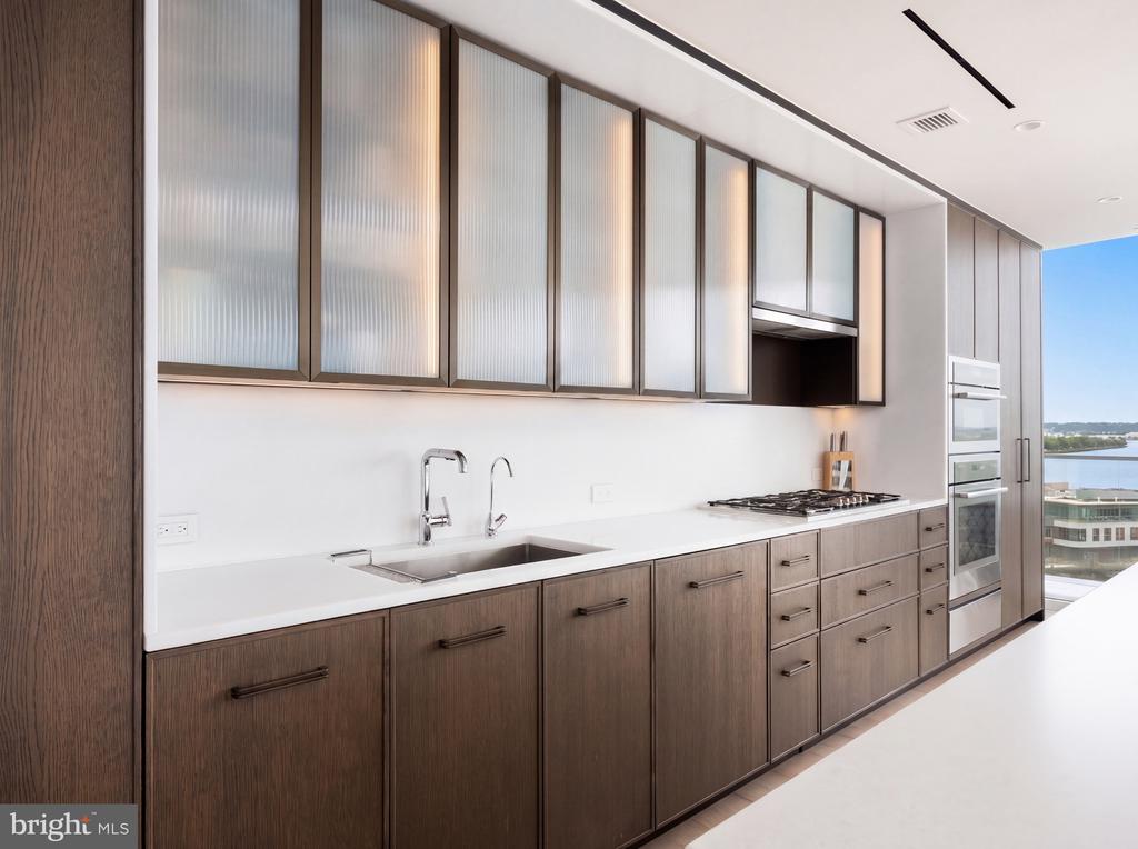Modern kitchen with dark wood cabinets, frosted-glass uppers, and water visible through the window.