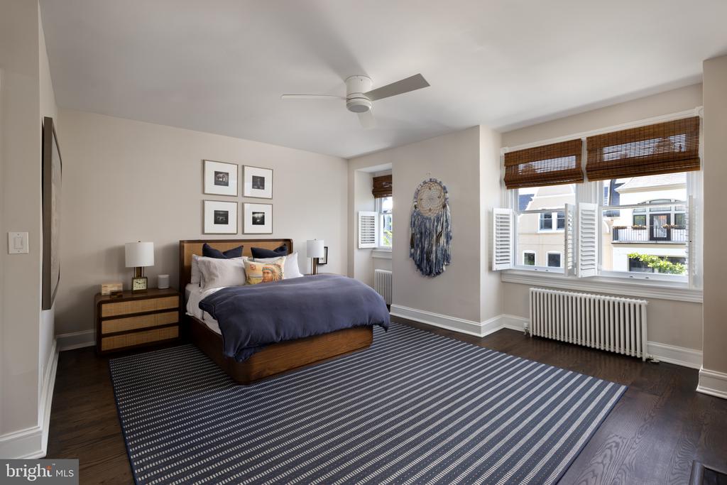 Bedroom with navy bedding, a striped rug, and large shuttered windows.
