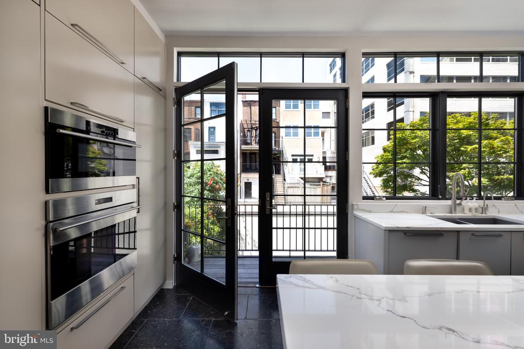 Modern kitchen with marble island, built-in double ovens, and an open balcony door.