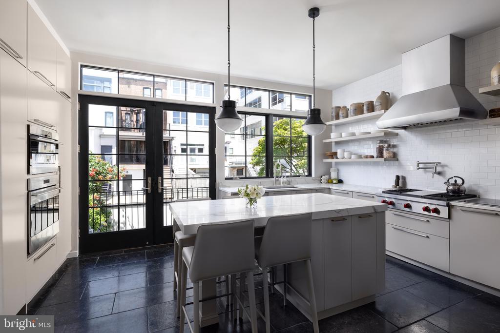 Bright kitchen with a large white island, black-framed glass doors, and a stainless steel gas range.