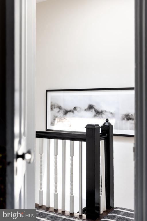 Staircase landing with black railing, white balusters, framed abstract artwork, and a patterned runner.