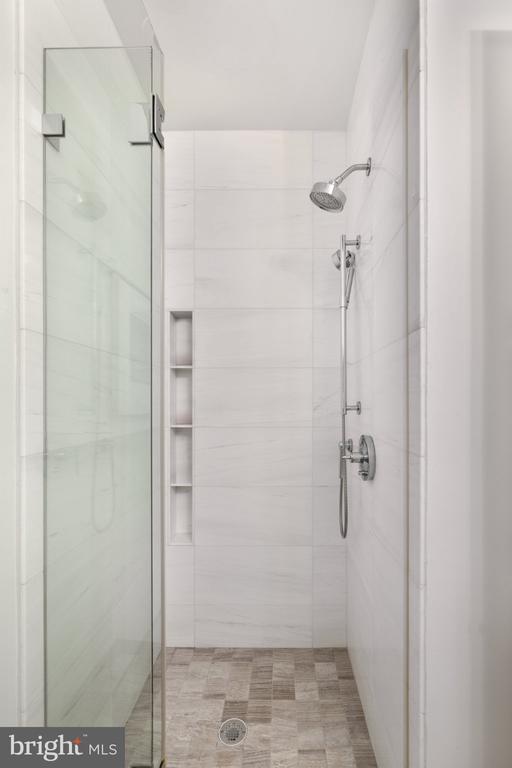 Walk-in shower with glass enclosure, white tile, built-in niche, and overhead and handheld showerheads.