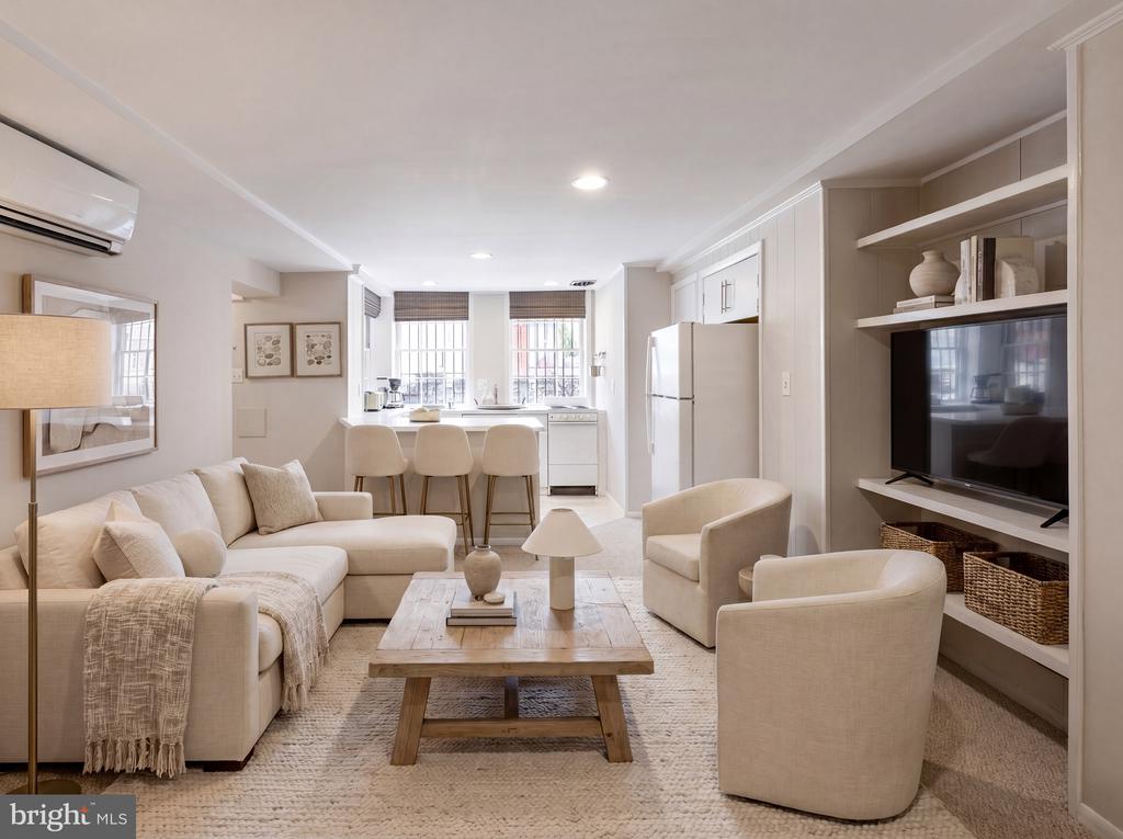 Living room with a cream sectional, two armchairs, and a wood coffee table beside the kitchen.