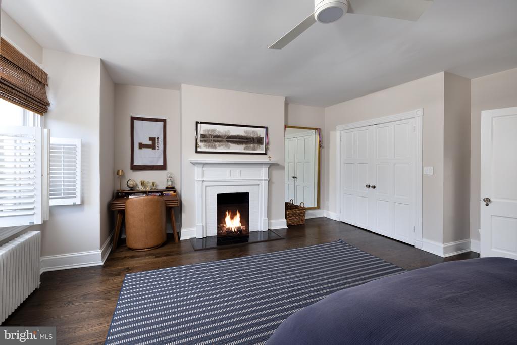 Bedroom with a lit fireplace, built-in closets, and a striped rug beside the bed.