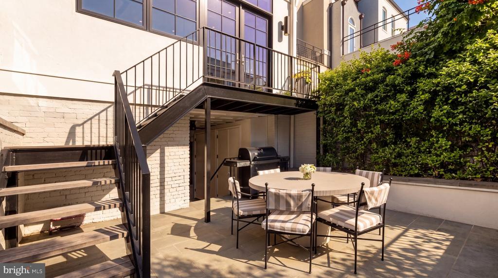 Private terrace with striped dining chairs, a round table, built-in grill, and metal staircase.