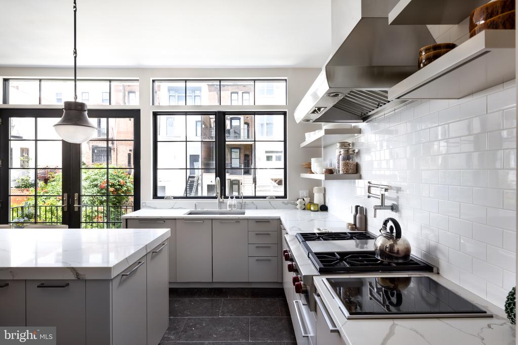 Modern kitchen with a large white island, stainless-steel range, and black-framed windows.