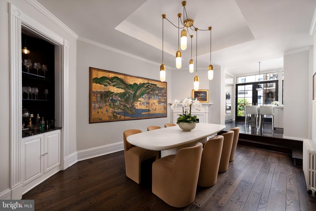 Dining room with an oval table, tan chairs, dark wood floors, and a large landscape painting.