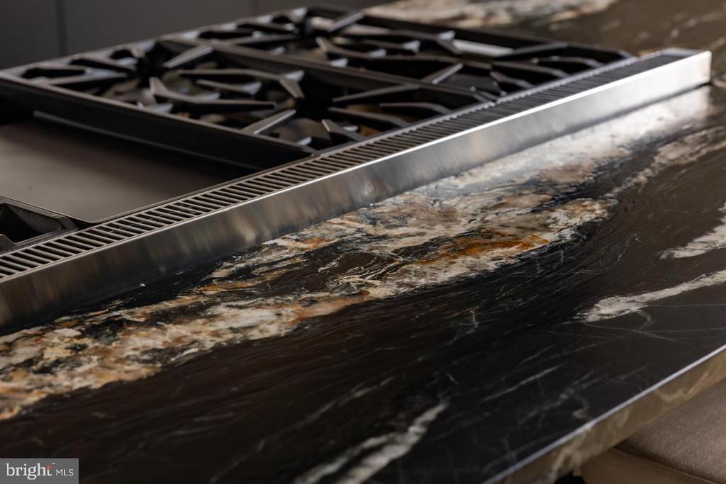 Kitchen gas cooktop beside a dark, dramatically veined stone countertop.