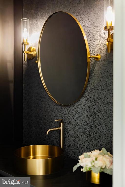 Bathroom vanity with a brass vessel sink, oval mirror, and matching wall sconces.