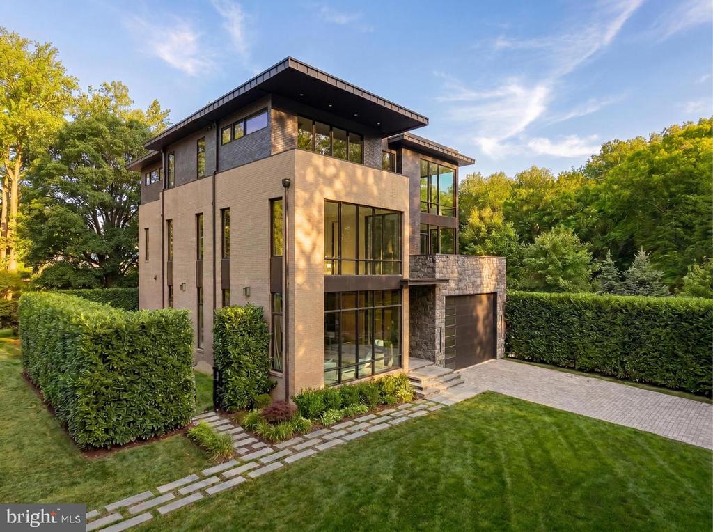 Modern brick-and-stone home with large windows, a landscaped lawn, and paved driveway.