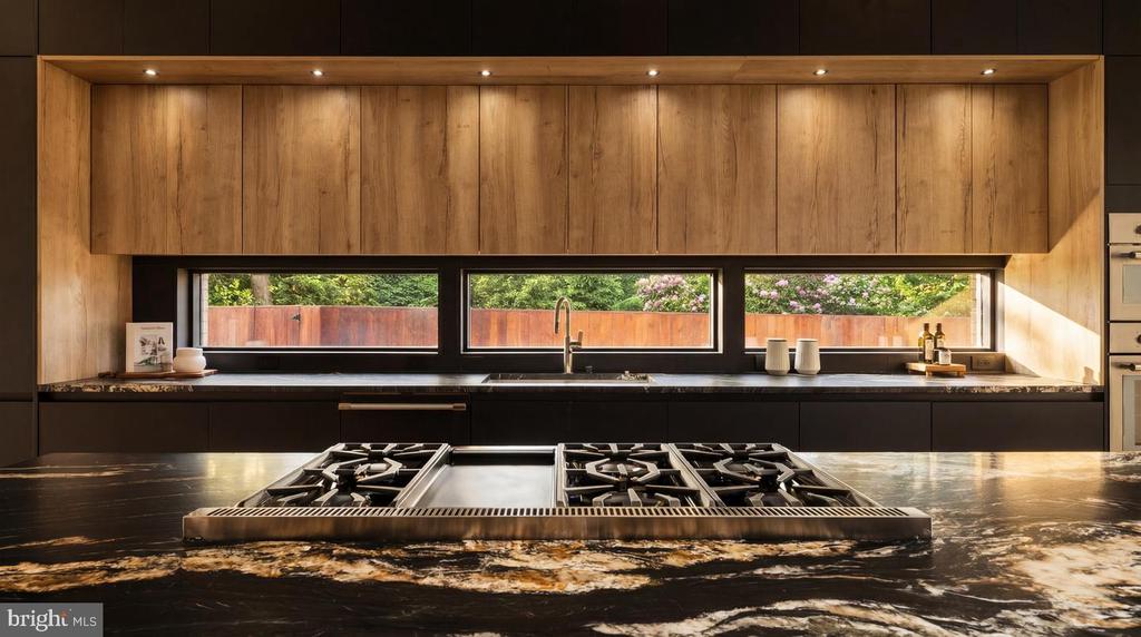 Modern kitchen with a black stone island, gas cooktop, warm wood cabinetry, and garden-facing sink window.