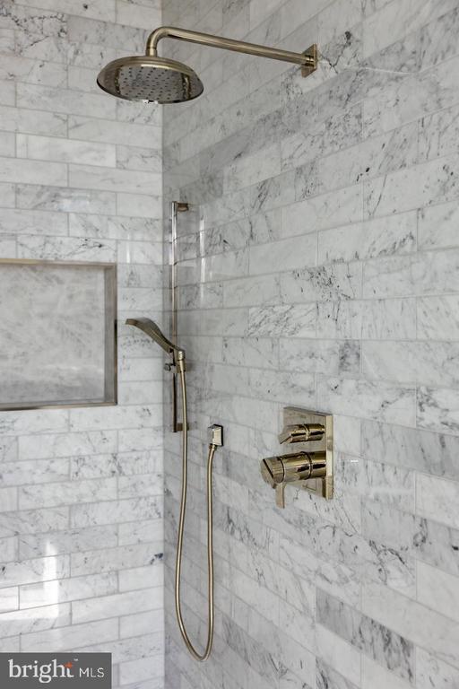 Marble-tiled shower with brass rainfall showerhead, handheld sprayer, and controls.