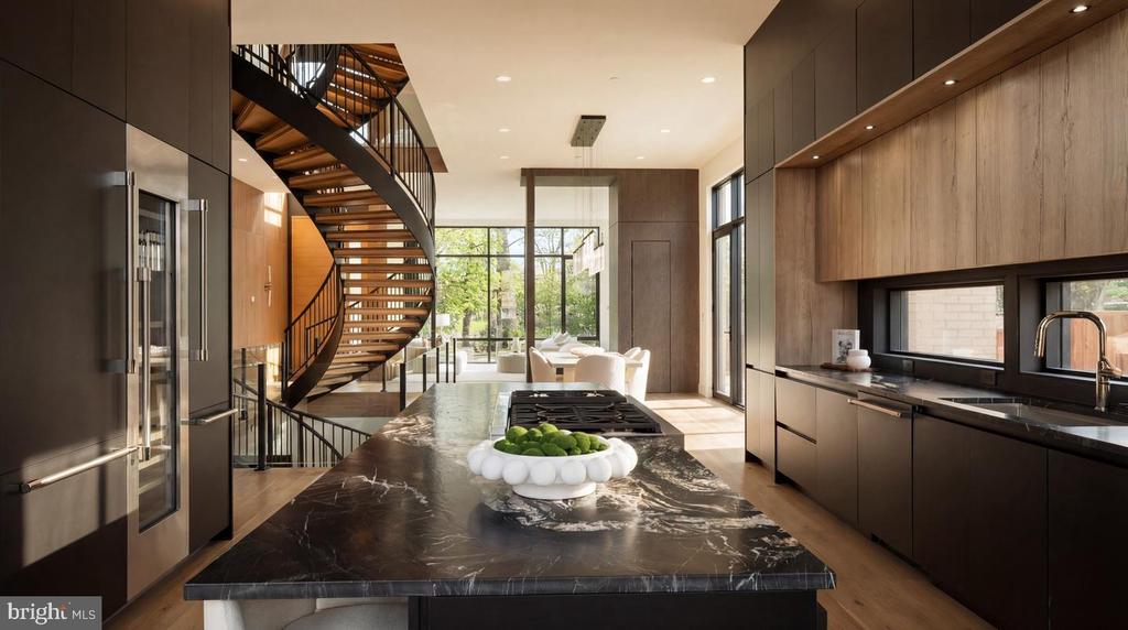 Modern kitchen with a dark marble island and dramatic curved staircase.