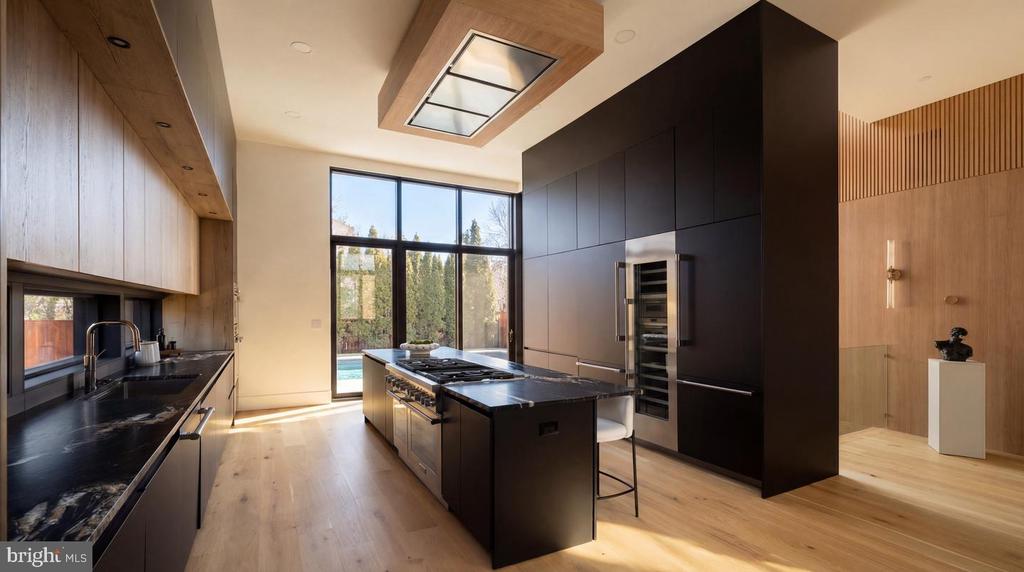 Modern kitchen with dark cabinetry and a large island, opening through tall windows toward a pool.
