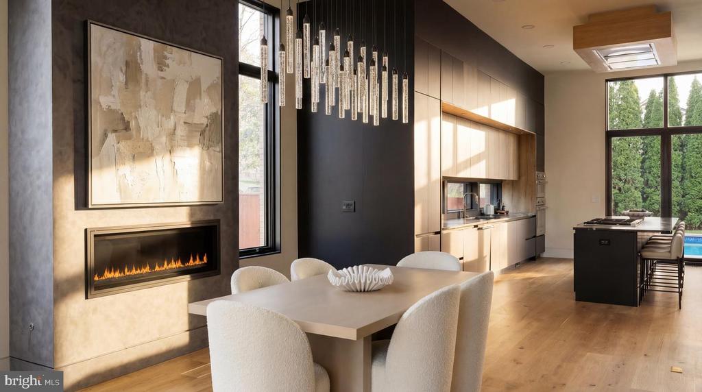 Modern kitchen and dining area with a black island, pale wood cabinets, and a linear fireplace.