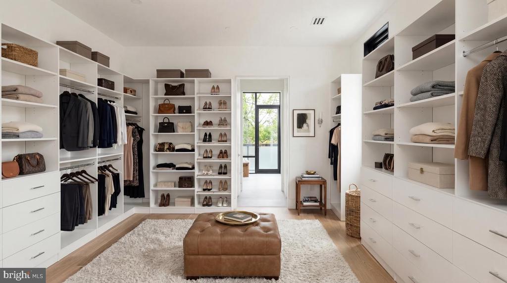 Walk-in closet with white built-ins, shoe shelves, hanging clothes, and a brown leather ottoman.