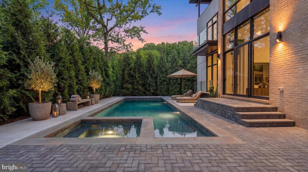 Modern home’s backyard pool and spa beside floor-to-ceiling windows at dusk.