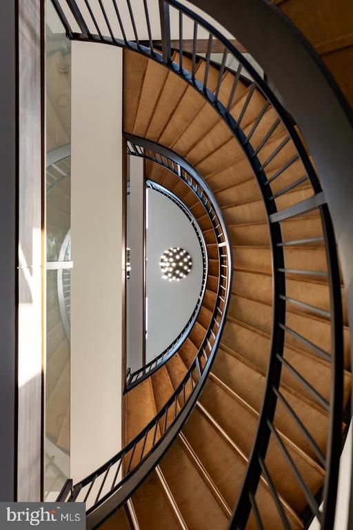 Curved wood staircase with dark metal railings viewed from below, with a chandelier above.