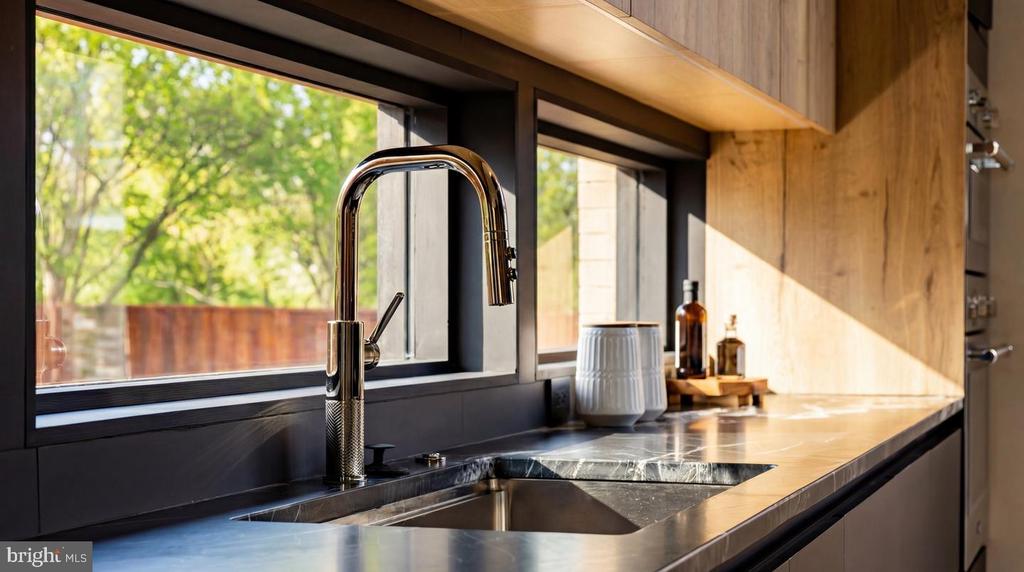 Modern kitchen sink with a tall chrome faucet, dark stone counter, and wide windows.