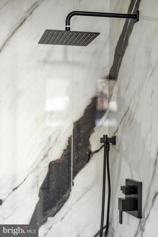 Marble shower with a black rain showerhead and matching handheld fixtures.