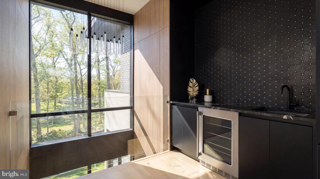 Modern kitchen bar with dark cabinetry, geometric backsplash, and a tall window overlooking leafy trees.