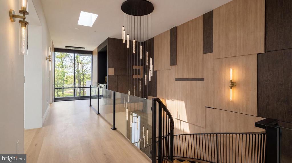 Modern hallway and landing with wood-paneled walls, glass railing, and curved staircase.