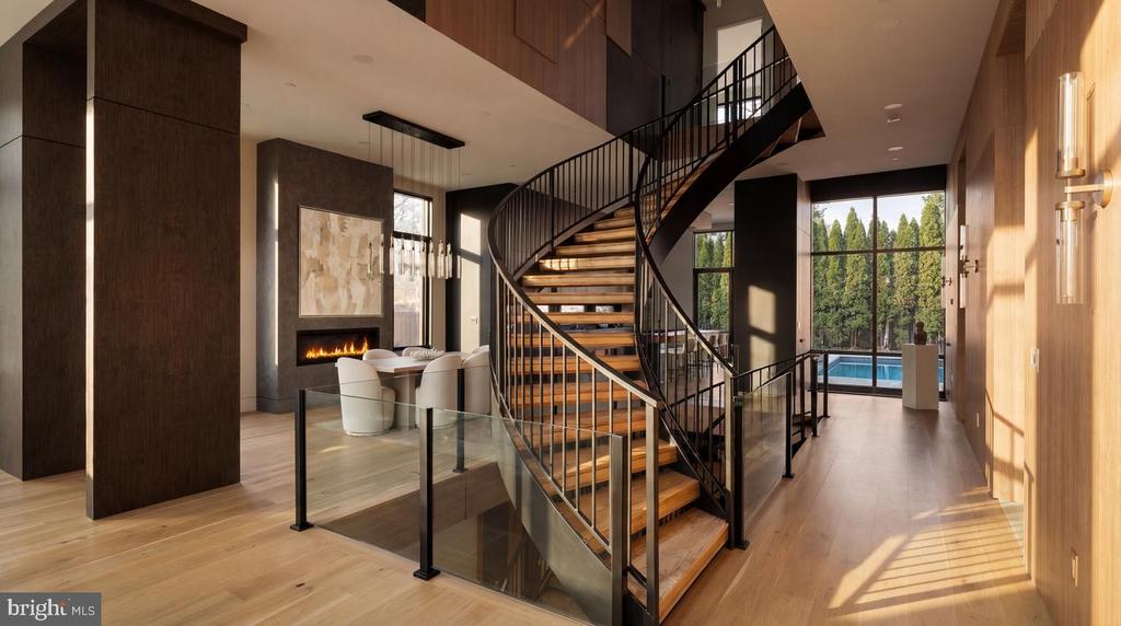 Modern foyer with a curved wood staircase, fireplace, and views of the pool through large windows.