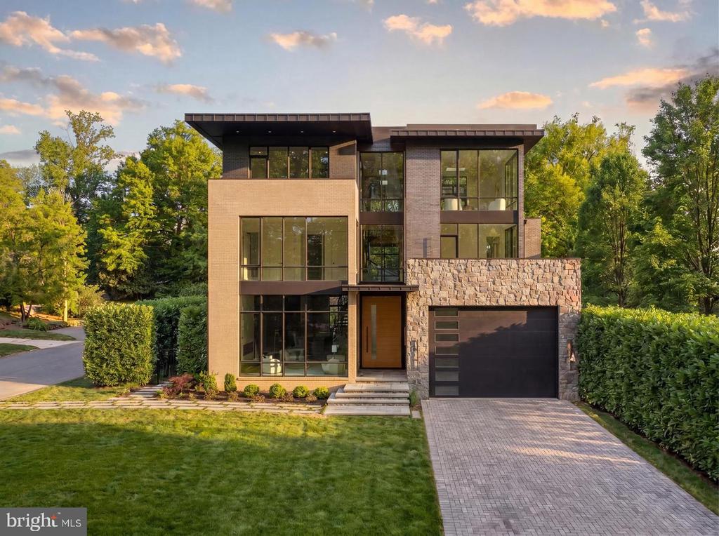 Modern home with floor-to-ceiling windows, a stone garage facade, and a paved driveway.