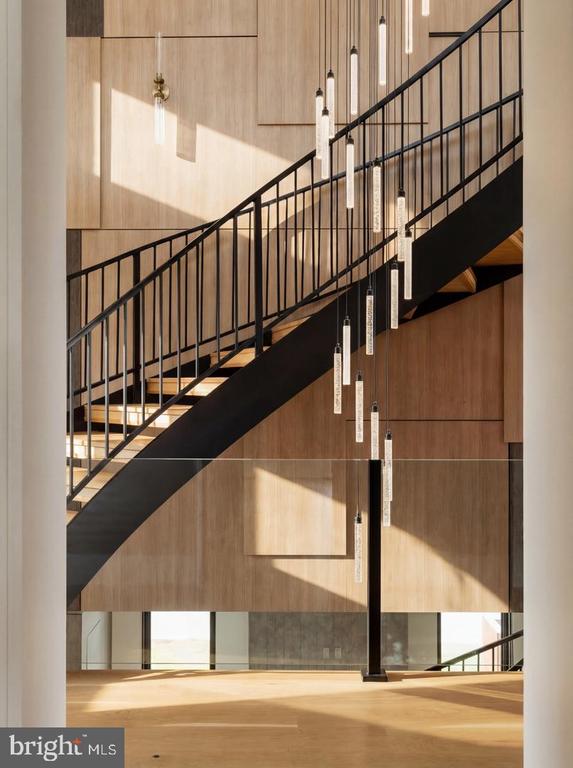 Sunlit foyer with a black metal staircase, wood-paneled walls, and slender pendant lights.