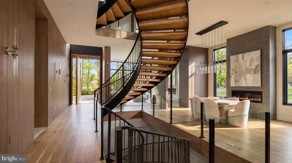 Open foyer with a dramatic wood staircase, glass railing, and dining area beside a linear fireplace.