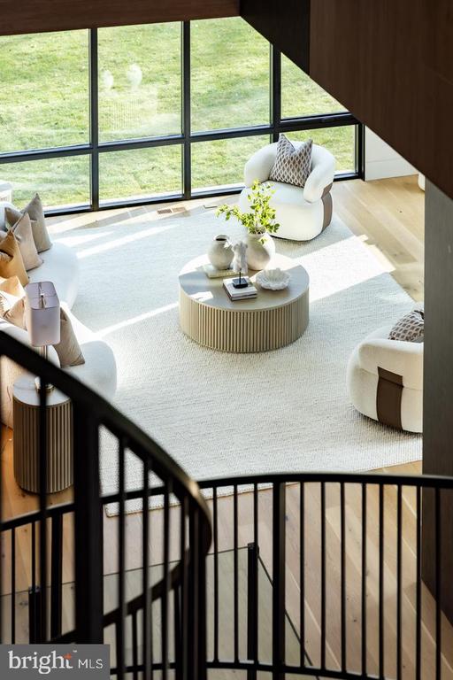 Staged living room with floor-to-ceiling windows, cream seating, and a curved staircase railing.