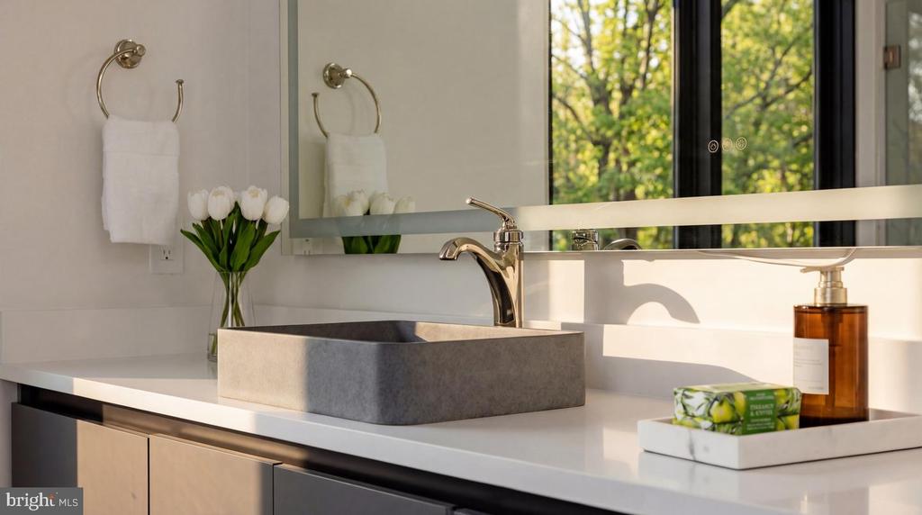 Bathroom vanity with a gray vessel sink, brass faucet, tulips, and a sunlit window.