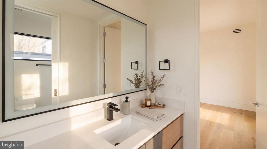 Bathroom vanity with a large mirror, black faucet, white countertop, and folded towels.