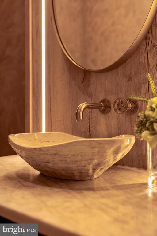 Stone vessel sink with a wall-mounted brass faucet and wood-paneled wall.
