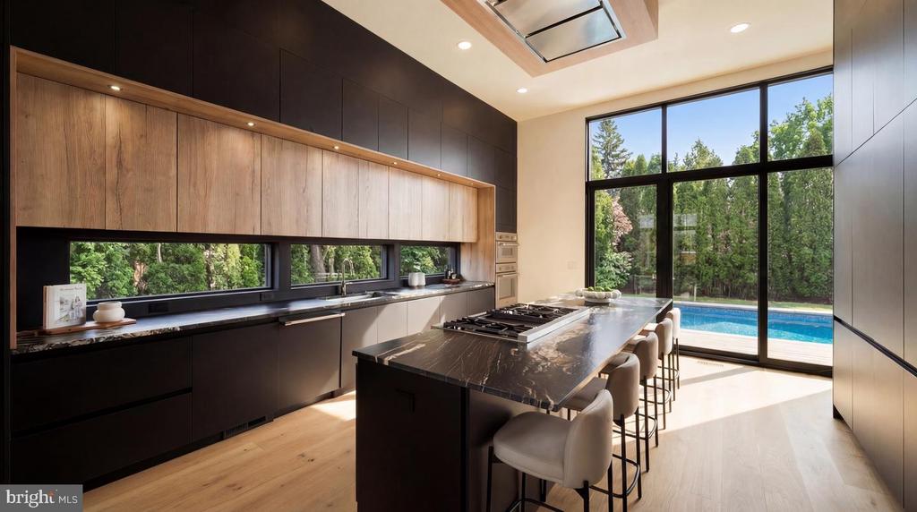 Modern kitchen with a marble island, dark cabinetry, and windows overlooking a pool.