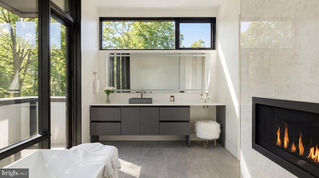 Modern bathroom with a freestanding tub, floating vanity, black-framed windows, and a lit fireplace.