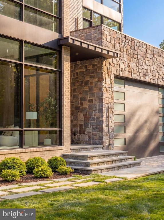 Modern home entrance with stone walls, broad glass windows, and landscaped front path.