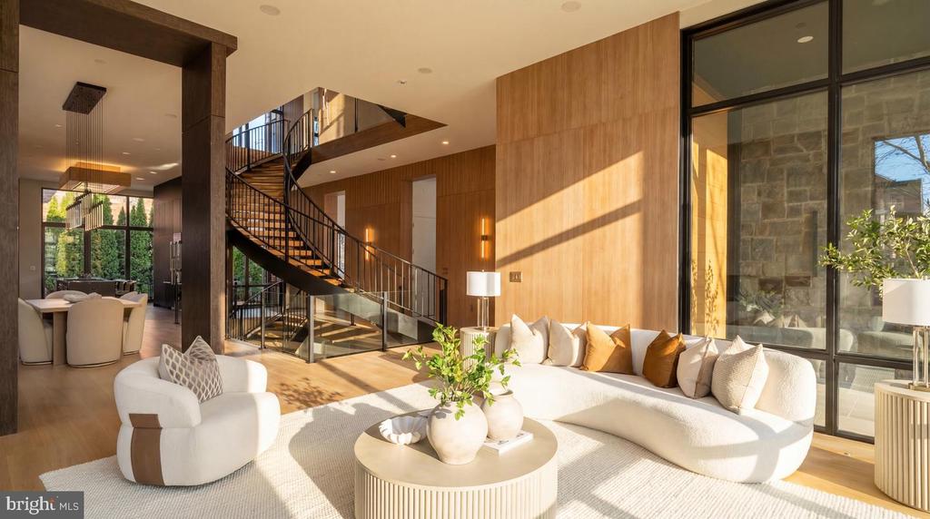 Living room with a white sectional, floor-to-ceiling windows, and a sculptural black staircase.
