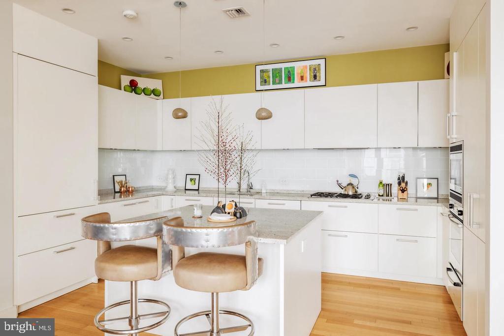 Modern white kitchen with a large island, upholstered bar stools, and light wood floors.