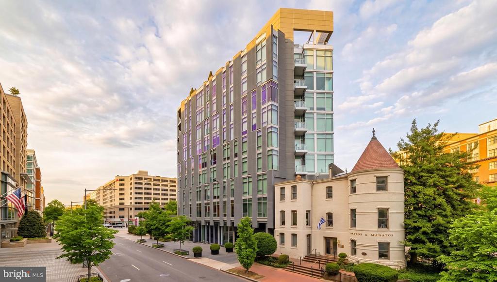 Modern gray-and-glass high-rise beside a historic building with a conical roof on an urban street.