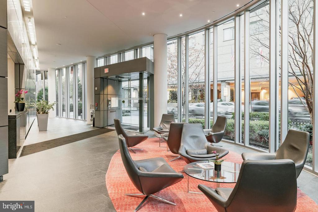 Condominium lobby with floor-to-ceiling windows, a glass entrance, and lounge seating on a coral rug.