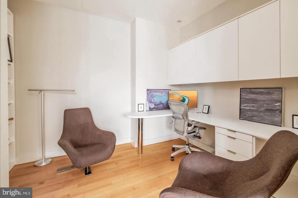 Home office with built-in white cabinetry, a long desk, and two upholstered lounge chairs.