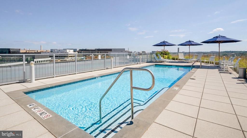 Rooftop pool with navy umbrellas, glass railings, and a distant city view.