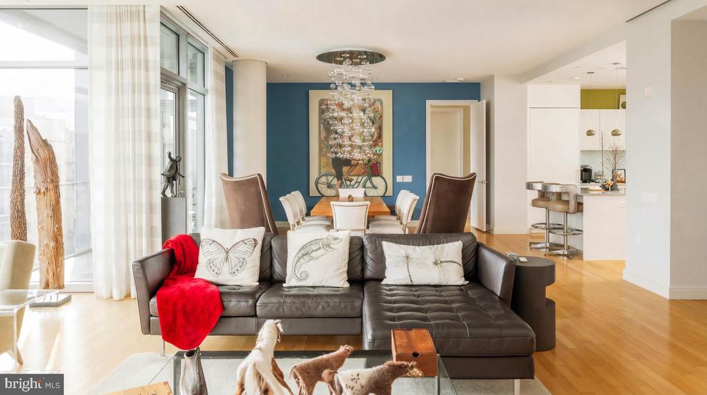 Living room with a leather sectional, red throw, floor-to-ceiling windows, and adjoining dining area.
