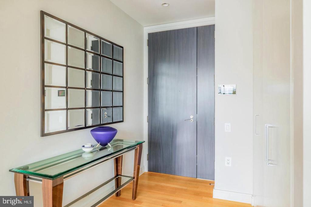 Entry foyer with a glass-top console, grid mirror, dark double door, and hardwood floor.