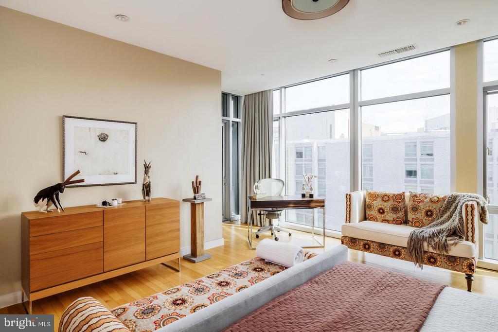 Condominium bedroom with a patterned sofa and floor-to-ceiling windows overlooking nearby buildings.